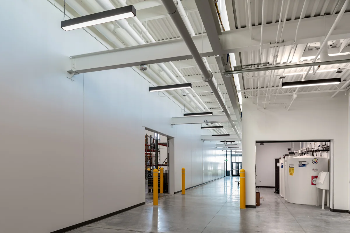 Service corridor with suspended lighting, exposed utilities, and protected openings.